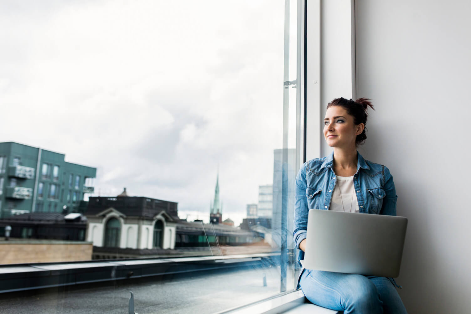 mujer con computador mirando por la ventana